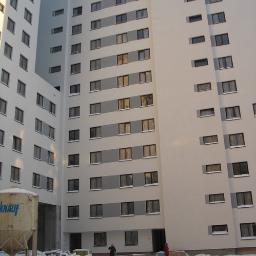 SQL biuro obsługi inwestycji - Wielopiętrowy budynek mieszkalny z oknami, widok z dołu na elewację z oknami, na pierwszym planie śnieg i dwie osoby, obok kontener Knauf.